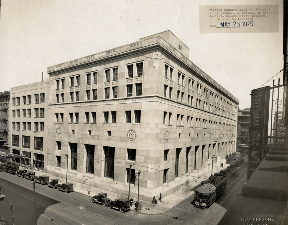 Cars are parked in front of two stone buildings at a downtown intersection in a black and white photo with a ‘May 25, 1925’ label in the top right corner.