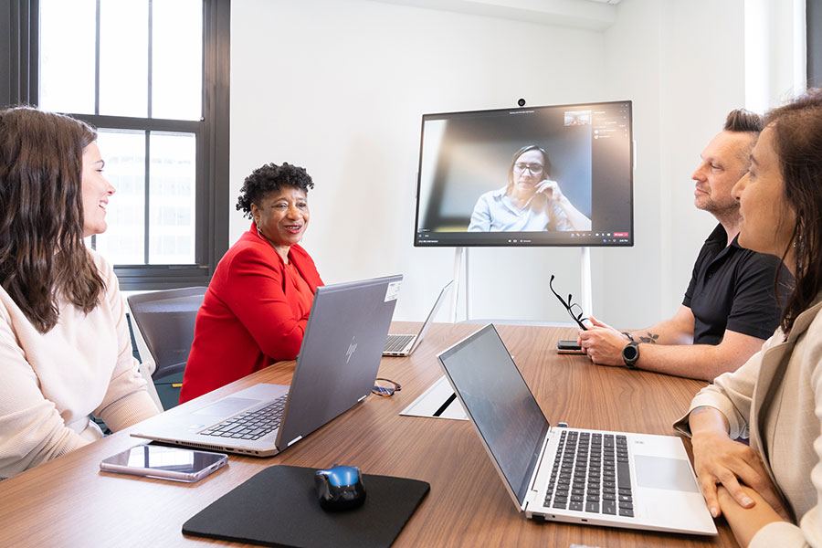 Four people seated at a conference table having a meeting with an employee participating virtually.