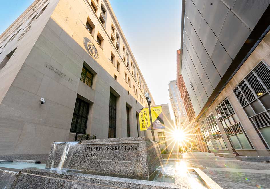 Morning sun glints across a plaza, illuminating a large taupe building in St. Louis.