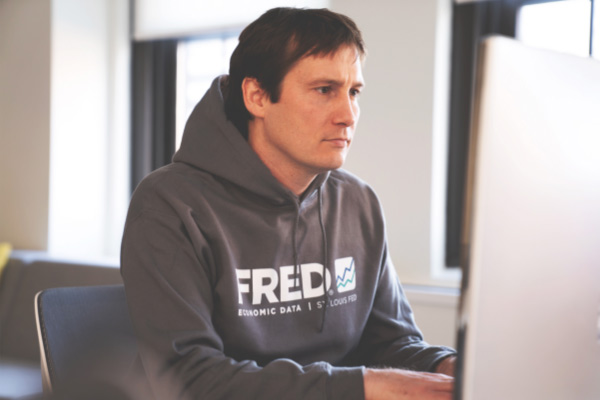 Man wearing FRED hoodie types on a computer.